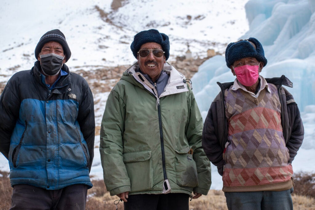 Three Ladakhi men stand in front of the ice stupa they built.