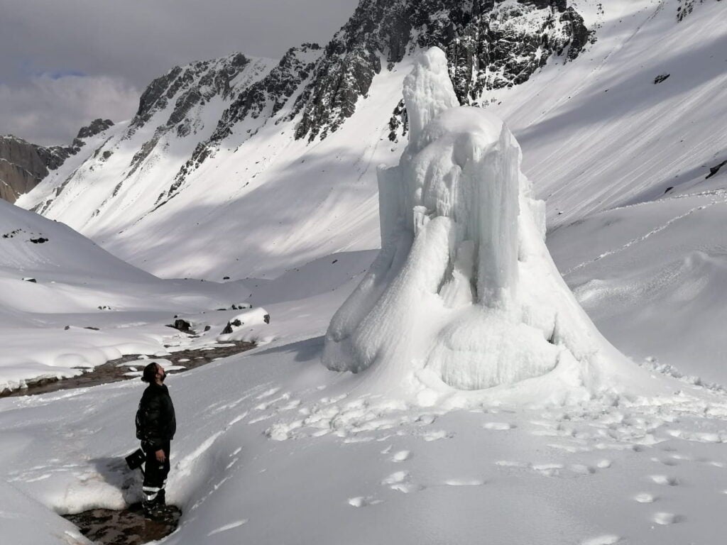 A Nilus team member stands in front of the first ice stupa built in Chile with a snow-covered Andes mountain range in the background.