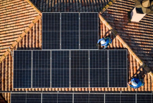 aerial view of Two workers installing solar panels on a house roof