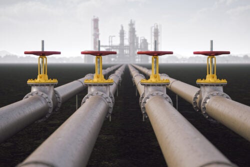 Pipelines with a refinery in the background amidst gray, cloudy skies.